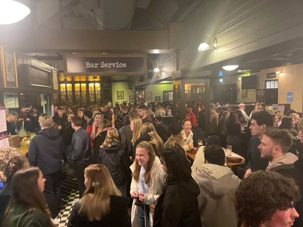 Photo of students in the Stables bar and restaurant. A sign saying 'Bar Service' is overhead.