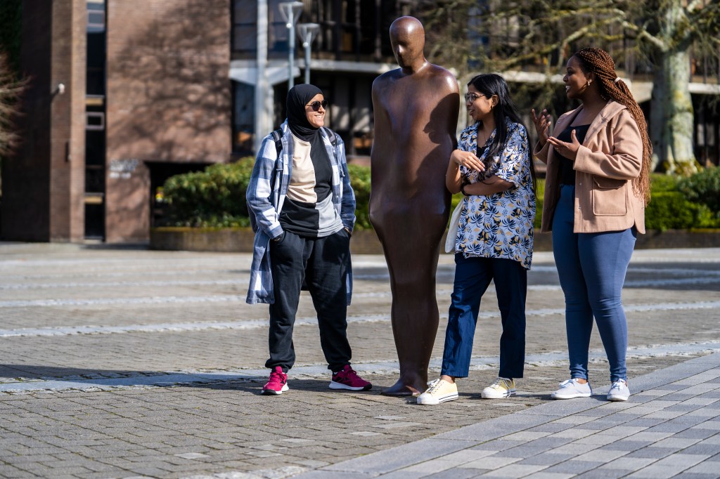 Photo of 3 students laughing and talking beside the Brown Thomas statue of UL