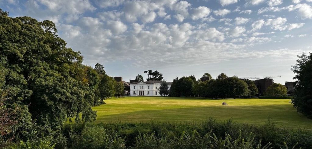 A distant photo of Plassey House on Campus surrounded by full green trees and a freshly cut green lawn 