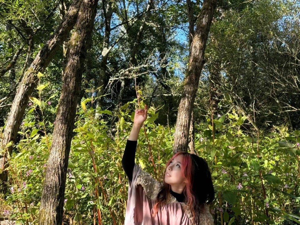 Niri, who has pink money pieces and dark hair holding her arm up in front of nature