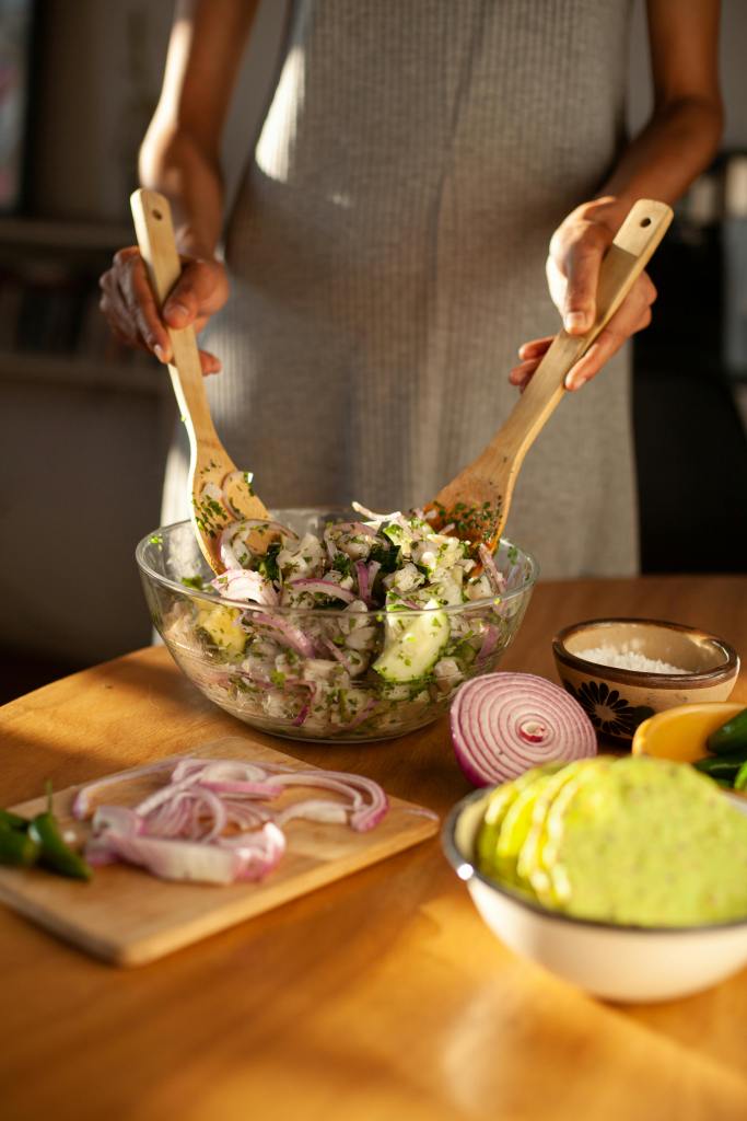 Someone tossing a salad with onions, cucumber and chillis