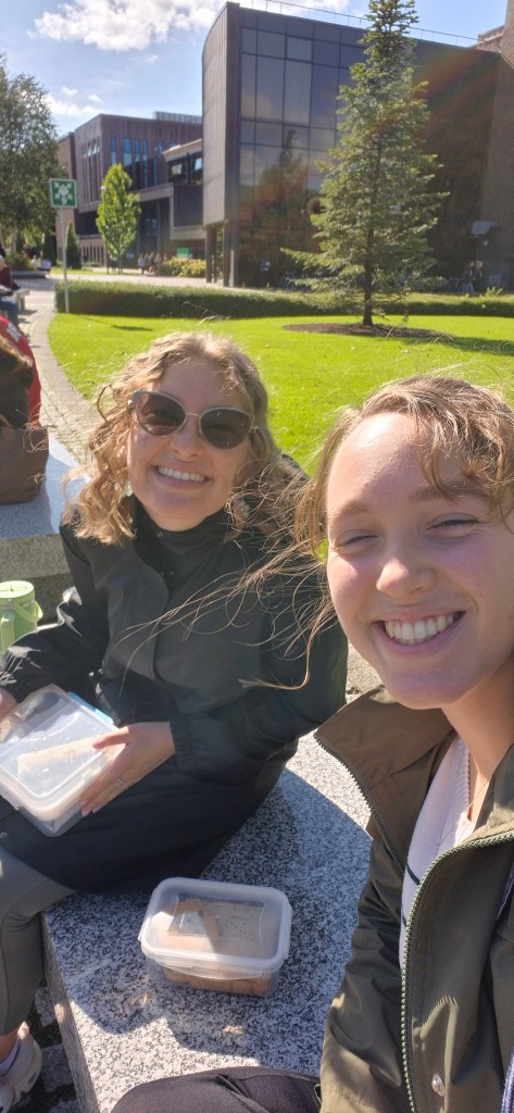 A selfie of Laura and a friend eating lunch on a bench