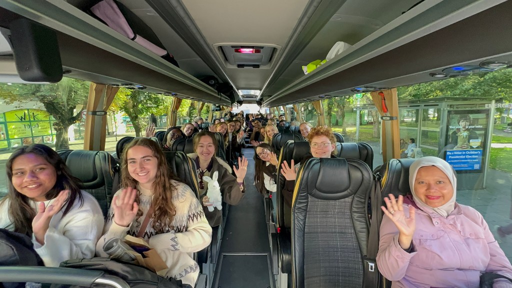 Ambassadors sitting on a bus and waving at the camera
