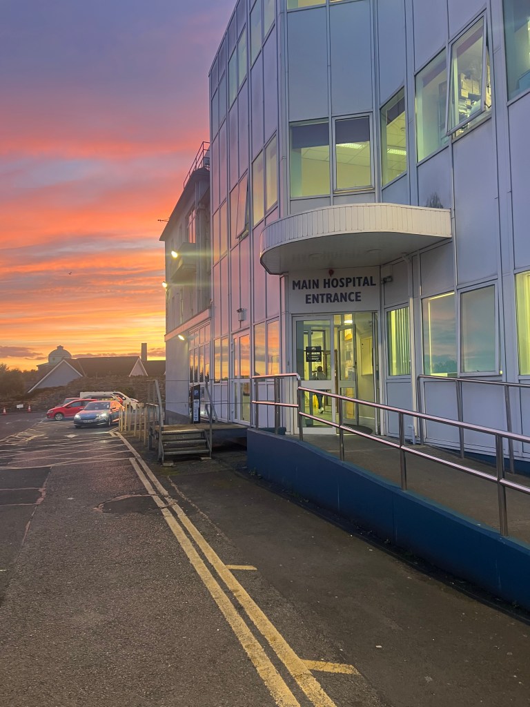 The outside view of the entrance of the Hospital. The background is a sunset.