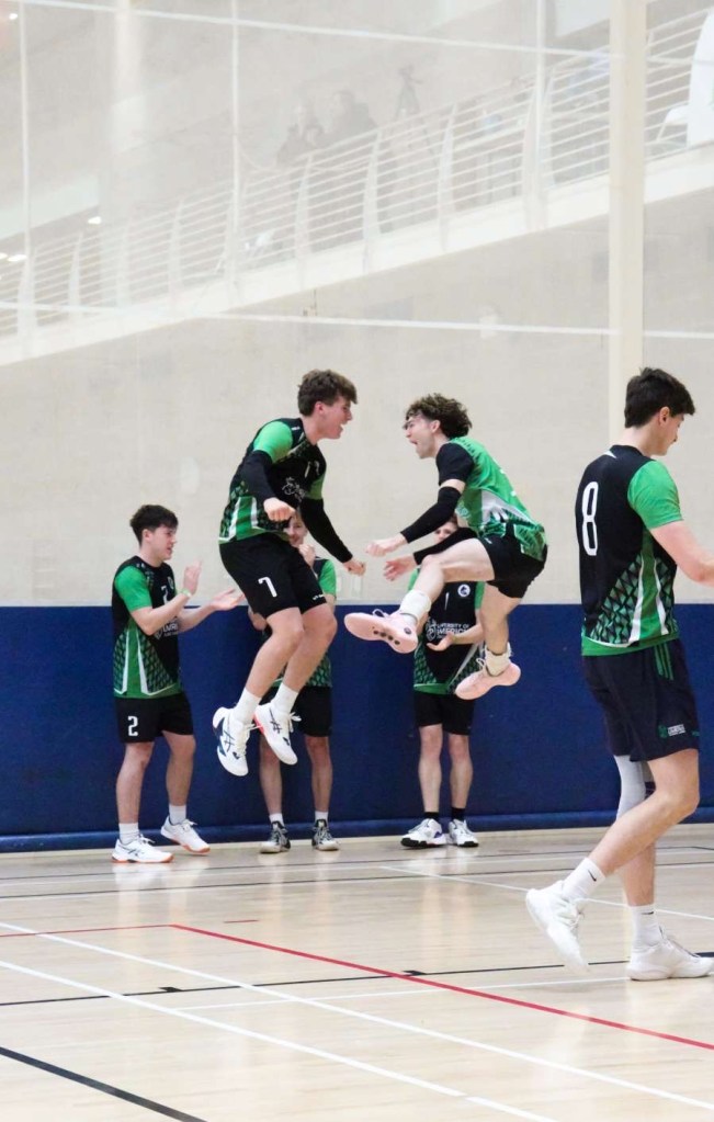 Image of Maddox and teammate jumping in the air on the court during a match.