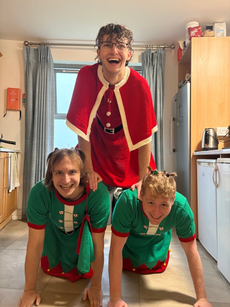 Image of Maddox and two friends wearing Christmas dresses for college Christmas whilst in a human pyramid.