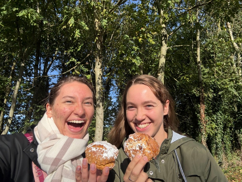 Selfie of Lauren and her roommate both enjoying a scone outdoors in sunny weather with nature in the background.